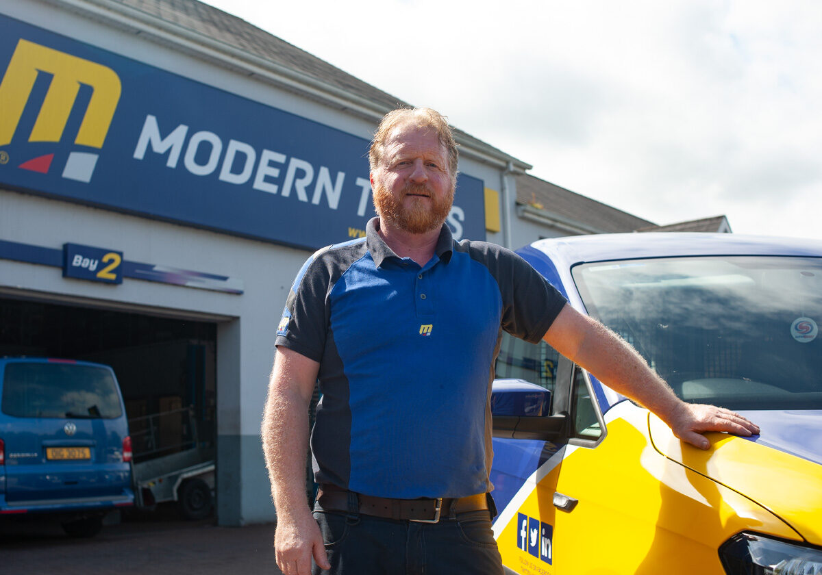 Modern Tyres team member beside a branded car at a depot